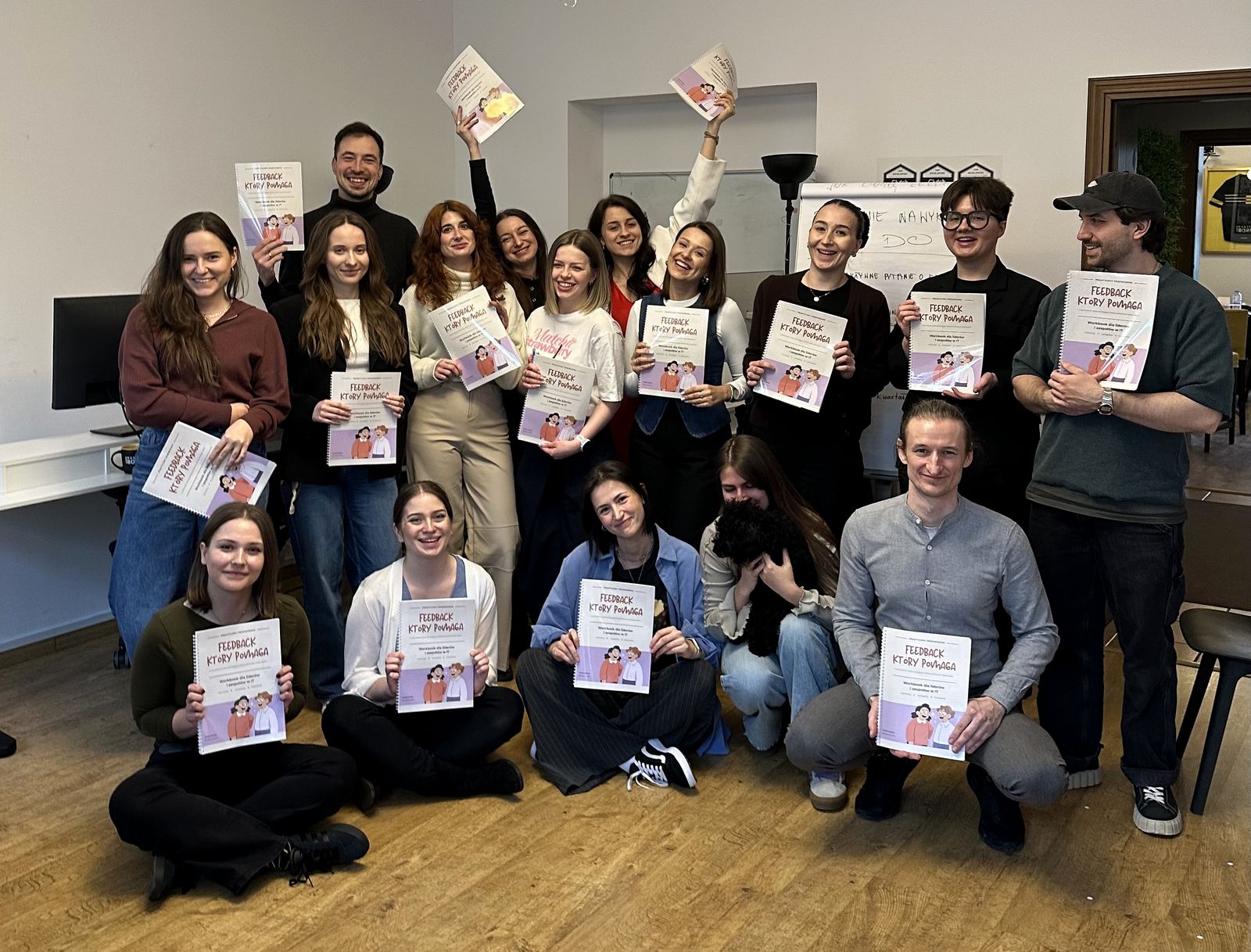 Uśmiechnięta grupa uczestników warsztatu z workbookami Feedback, który pomaga